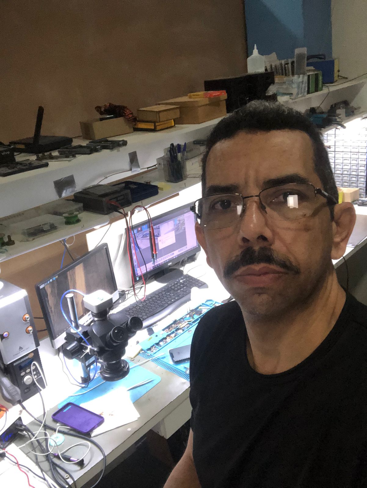 Técnico da JLG INFOCELL na bancada de manutenção com microscópio e equipamentos